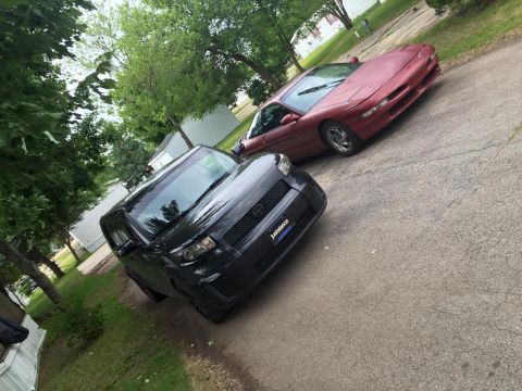 1995 Ford Probe - A red Ford Probe and a black Scion xB are parked on a cracked asphalt driveway.