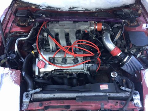 1995 Ford Probe - The V6 engine bay features red spark plug wires and an aftermarket air intake, with snow visible on the vehicle's exterior.