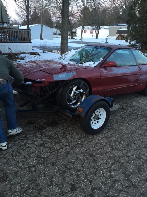 1995 Ford Probe - A red 1995 Ford Probe is being loaded onto a trailer, with visible damage to the front end.