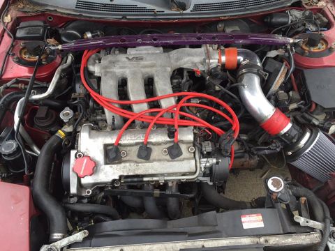 1995 Ford Probe - Engine bay view of a V6 engine with red spark plug wires and an aftermarket air intake system.