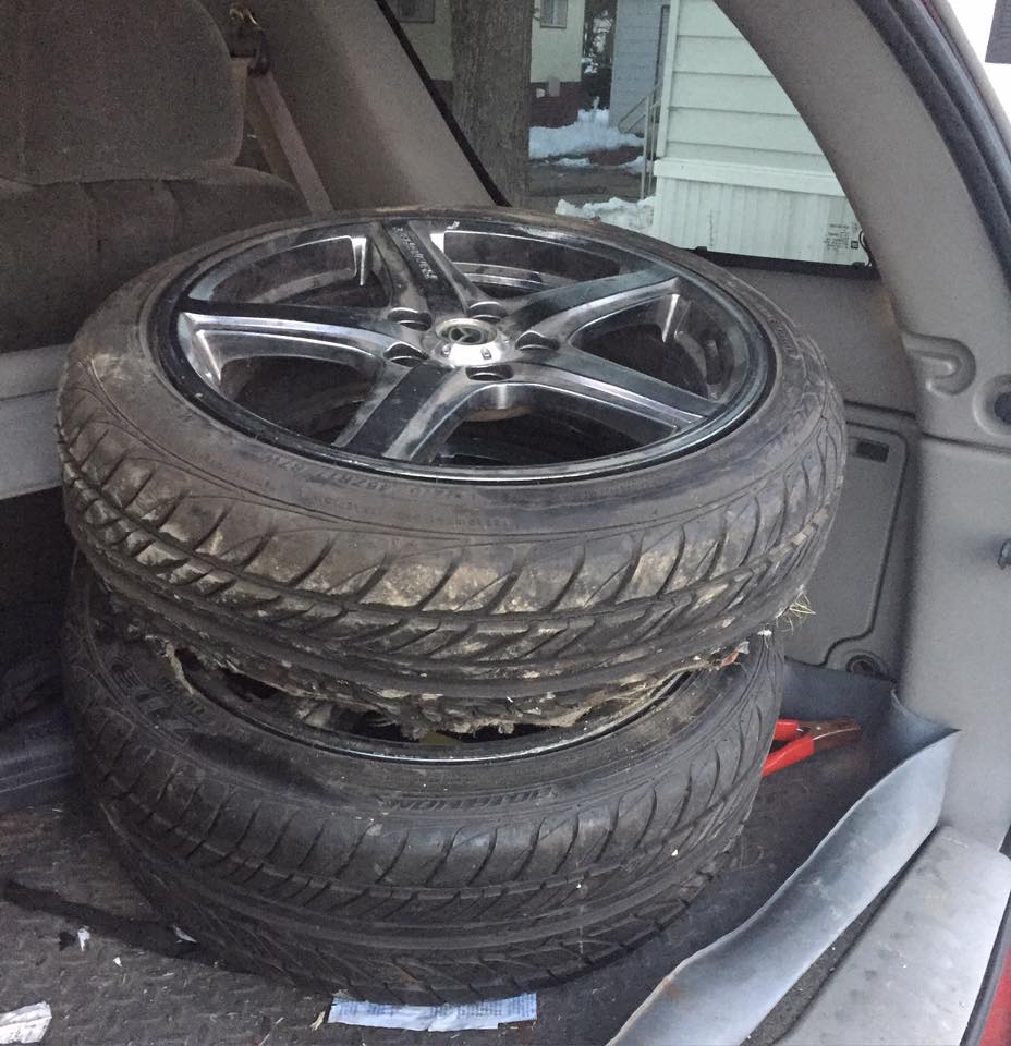 Two used tires stacked on aftermarket rims inside a vehicle's cargo area