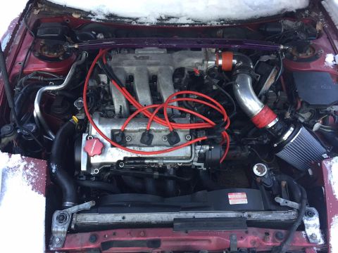 1995 Ford Probe - The engine bay of a red car, a V6 engine with red spark plug wires and an aftermarket air intake system.