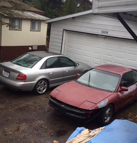 1995 Ford Probe - Two cars are parked in a driveway next to a garage and a small building.