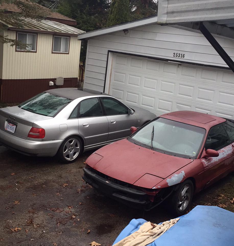 Red sports car with pop-up headlights parked next to a silver sedan in a driveway