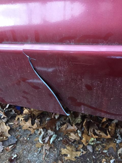 1995 Ford Probe - The trim on the lower body panel of a red vehicle has come loose and is peeling away.
