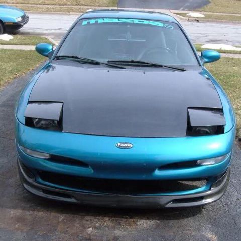 1995 Ford Probe - Teal Mazda Probe with pop-up headlights visible from the front, another vehicle partially seen in the background.