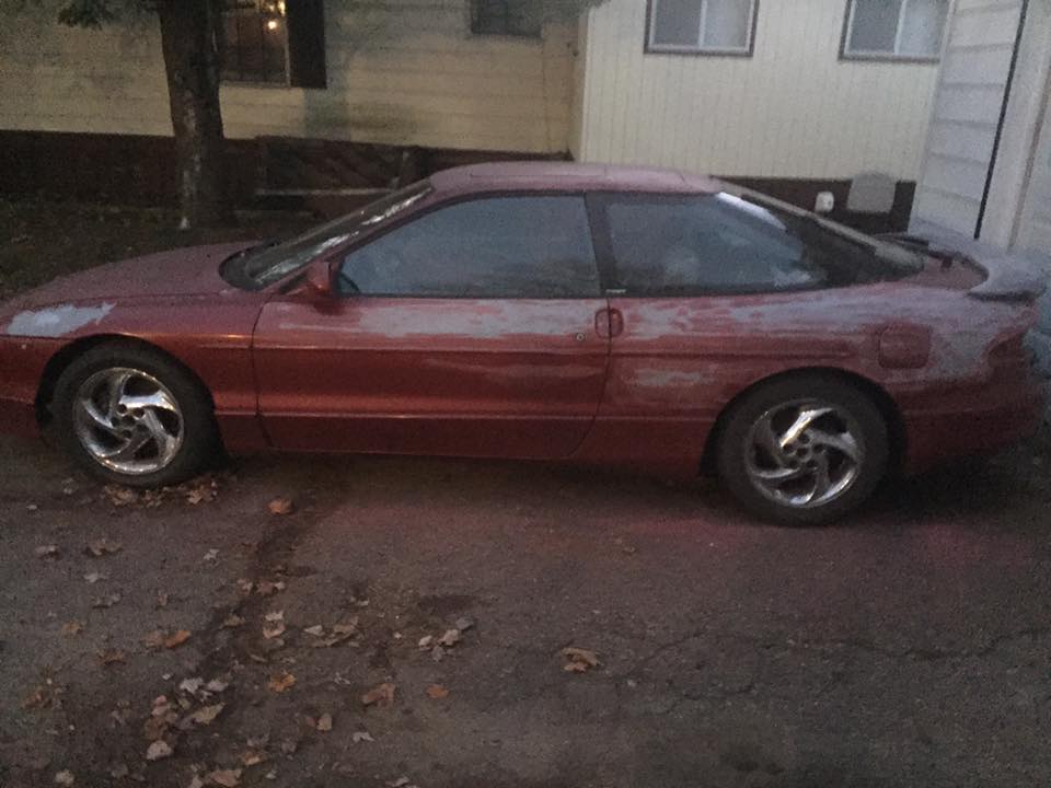 Side view of a red 1995 Ford Probe with primer showing through the paint