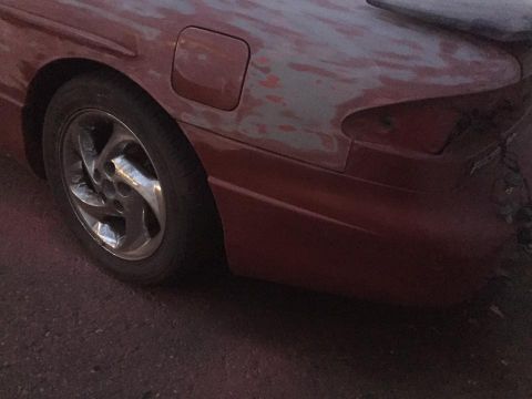 1995 Ford Probe - Rear quarter panel of a faded maroon coupe with peeling clearcoat and a chrome alloy wheel, shot in low light.