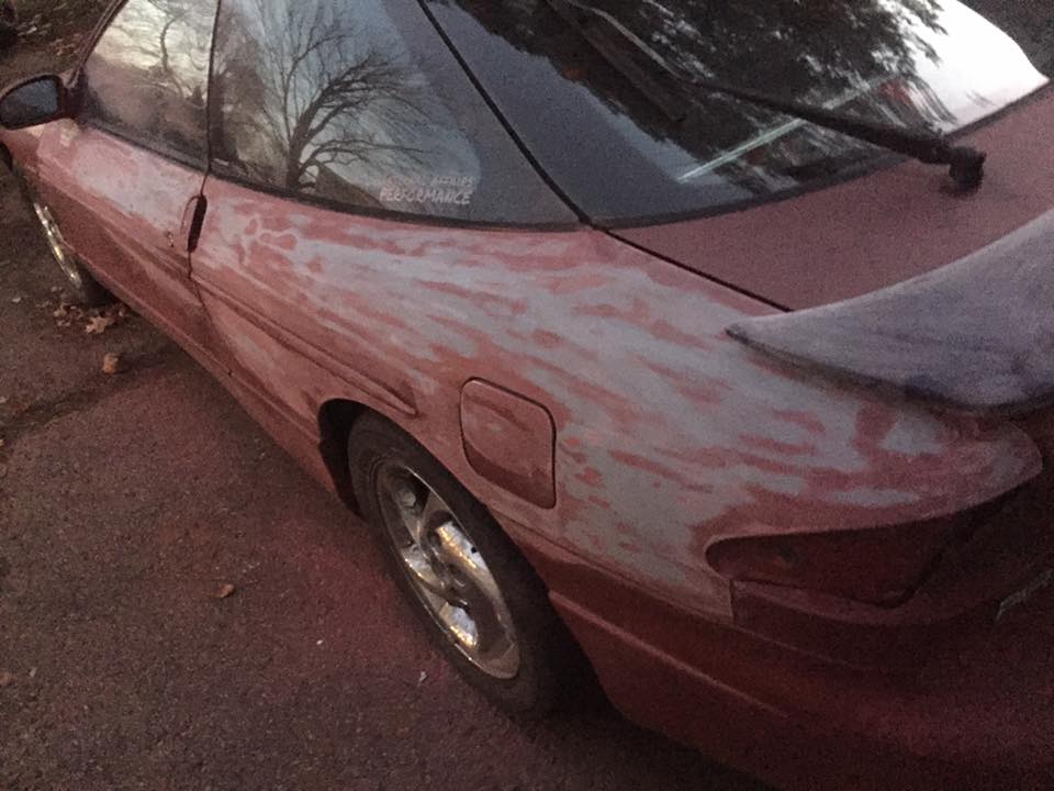 Red car, primer patches on rear quarter panel, side view