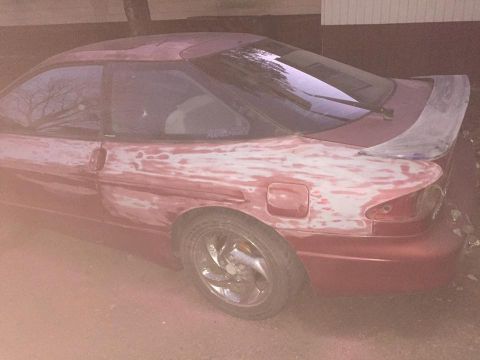 1995 Ford Probe - This red coupe, possibly a Ford Probe, is undergoing bodywork with visible filler on its side.