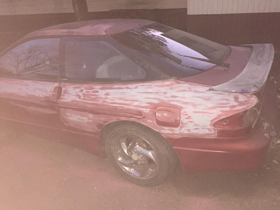 red coupe, looks like a Ford Probe, with body filler on the side and a spoiler
