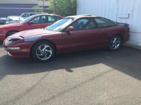 1995 Ford Probe - A red 1995 Ford Probe coupe is parked next to another red car, with a white building in the background.