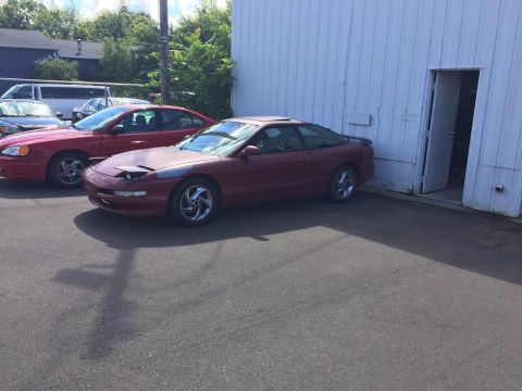 1995 Ford Probe - A red 1995 Ford Probe is parked outside a building, with another red car beside it.