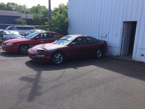 1995 Ford Probe - A maroon 1995 Ford Probe is parked next to a red sedan in front of a white building.