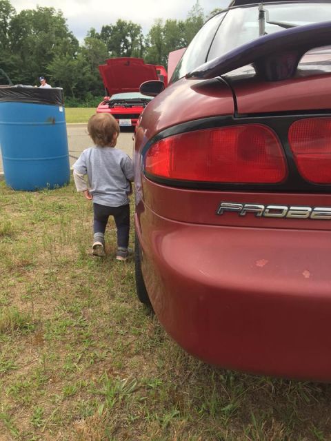 1995 Ford Probe - A child stands near the rear of a red car, with another car visible in the background.