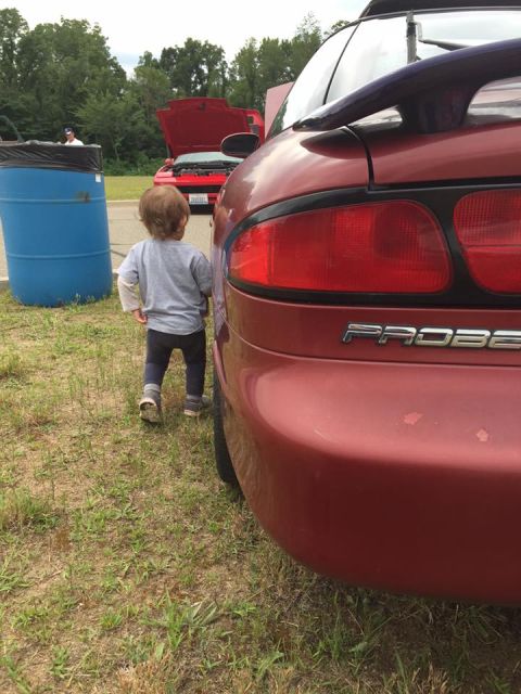 1995 Ford Probe - A child walks past the rear of a red Ford Probe, with another red car visible in the background.