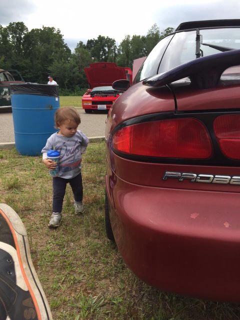 1995 Ford Probe - A child stands next to a red Ford Probe, with another red car visible in the background.