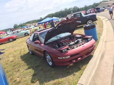 1995 Ford Probe - A red coupe, likely a third-generation Ford Probe, is displayed with its hood open at an outdoor car show.