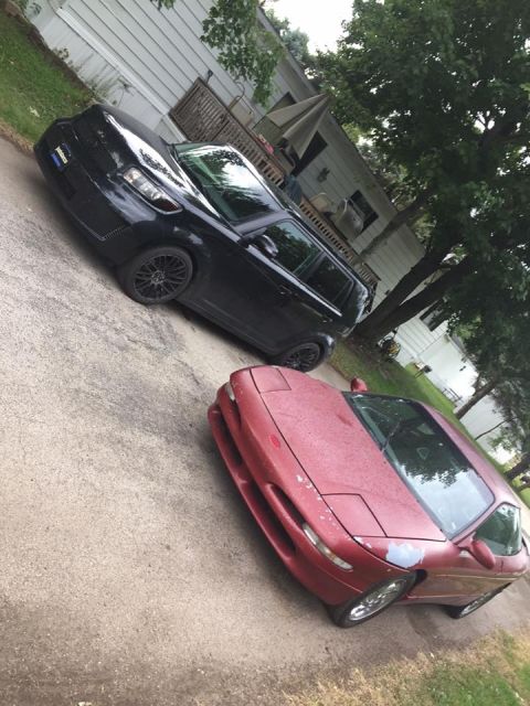 1995 Ford Probe - A red sports car and a black SUV are parked on a driveway in front of a house.