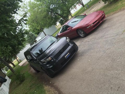 1995 Ford Probe - Two vehicles are parked on a driveway in front of houses and trees.