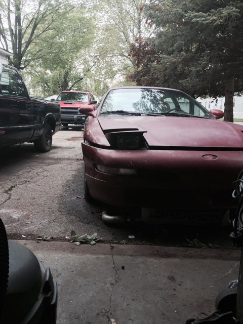 1995 Ford Probe - A maroon 1995 Ford Probe is parked in a driveway next to a black pickup truck. The Probe's hood is open, revealing the front of the car wit…