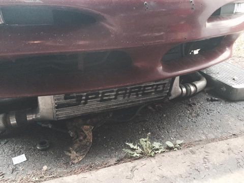1995 Ford Probe - A close-up, low-angle view of the front bumper area of a dark red vehicle, revealing a large aftermarket intercooler with the word "SPEARCO…