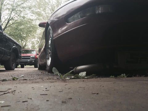 1995 Ford Probe - Low angle shot of the rear of a red Ford Probe, showing the exhaust pipe and a portion of the rear tire. A black pickup truck and a red Che…