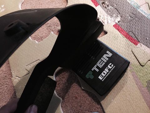 1995 Ford Probe - A black TEIN EDFC Electronic Damping Force Controller is mounted to a black plastic bracket, resting on a textured surface.