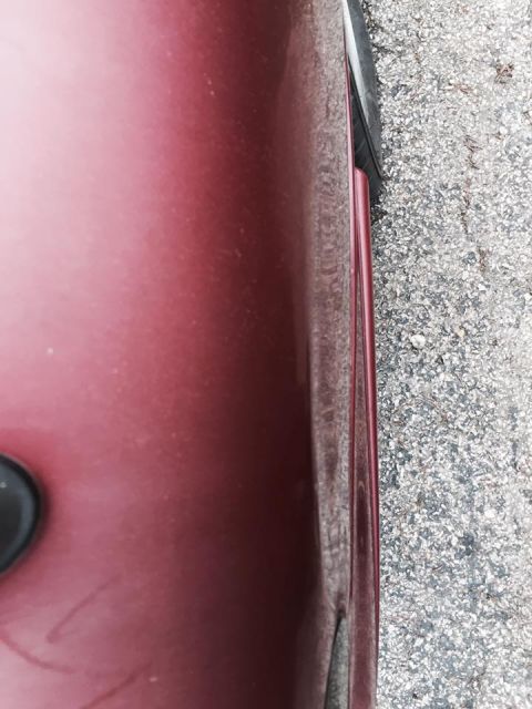 1995 Ford Probe - A close-up side view of a dark red vehicle's body panel next to a gravel surface. The vehicle appears to be a sedan or coupe.