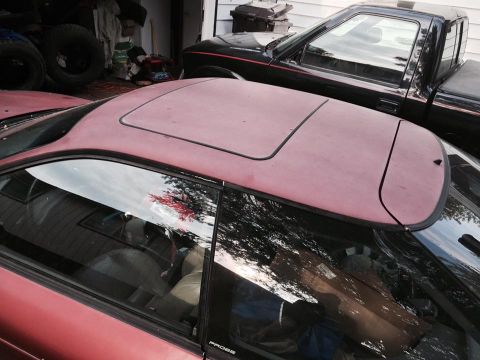 1995 Ford Probe - A close-up, slightly elevated view shows the maroon roof and passenger side window of a 1990s coupe, with a black pickup truck visible behi…