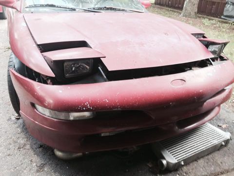 1995 Ford Probe - The front end of a red Ford Probe is shown, with its hood open and pop-up headlights partially raised. An intercooler is visible underneath…