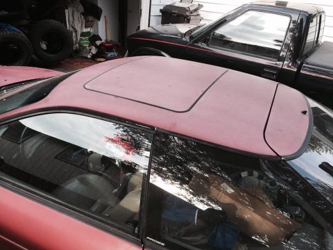 1995 Ford Probe - A close-up, high-angle view of the sunroof and roof of a red coupe, with a black pickup truck visible in the background.