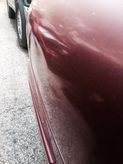 1995 Ford Probe - Close-up side view of a dark red vehicle's fender and wheel well. The vehicle appears to be parked on a paved surface next to another vehic…