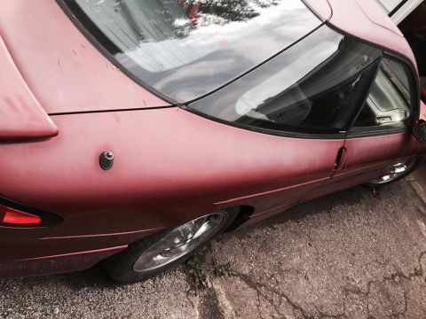 1995 Ford Probe - A close-up, side view of a dark red 1995 Ford Probe shows the rear quarter panel, window, and wheel. The car is parked on a cracked concret…