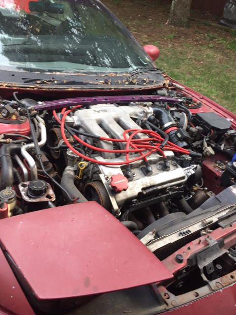 1995 Ford Probe - The engine bay of a red 1995 Ford Probe is shown with the hood open, revealing the V6 engine and various engine components. The car is park…