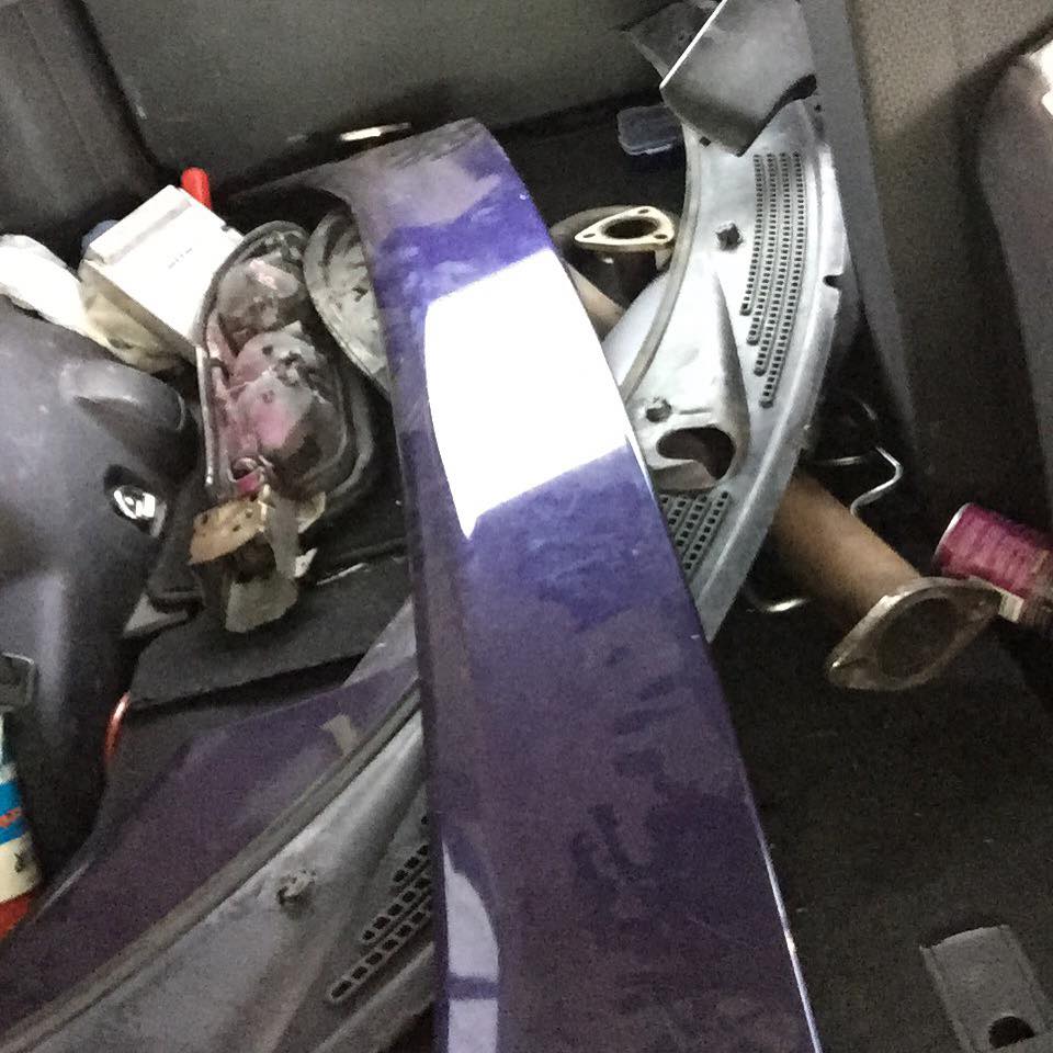 Purple car part in foreground, with car parts like exhaust pipes in background.