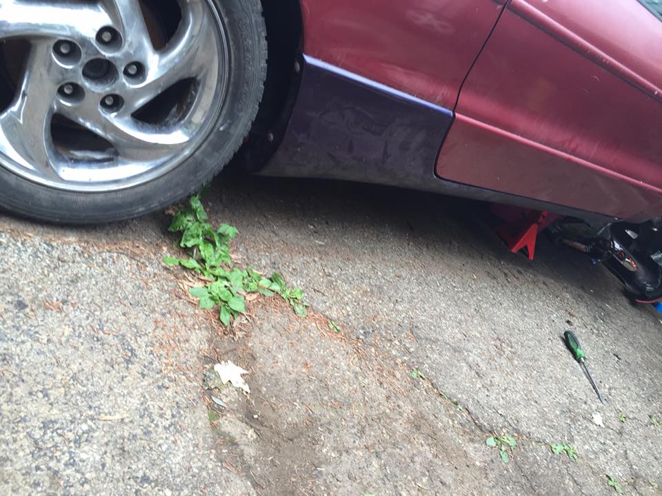 Red car's side panel and wheel, with jack stand and screwdriver on ground.
