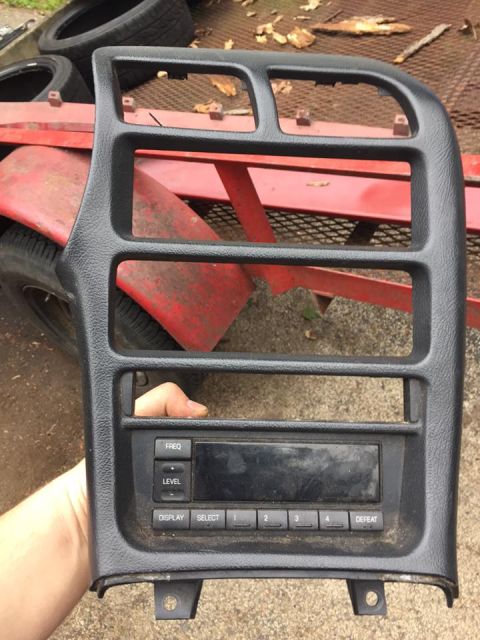 1995 Ford Probe - A person holds a black car radio and dash trim piece. The trim has several openings and the radio features a digital display and buttons la…