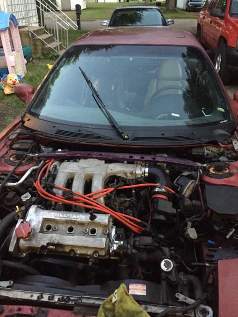 1995 Ford Probe - The engine bay of a red Mazda Probe is shown, with the hood open. The engine has orange spark plug wires and a silver intake manifold.
