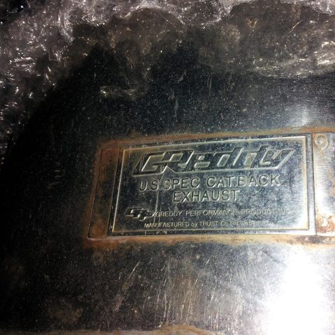 1995 Ford Probe - A close-up shot of a metal plaque on a vehicle part, featuring the GReddy logo and text indicating "U.S. SPEC CATBACK EXHAUST" and "MANUFAC…
