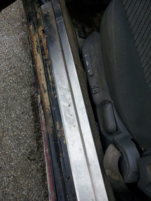 1995 Ford Probe - This is a close-up interior view of a car's driver's side door sill and seat controls. The door sill shows significant rust and wear, while…