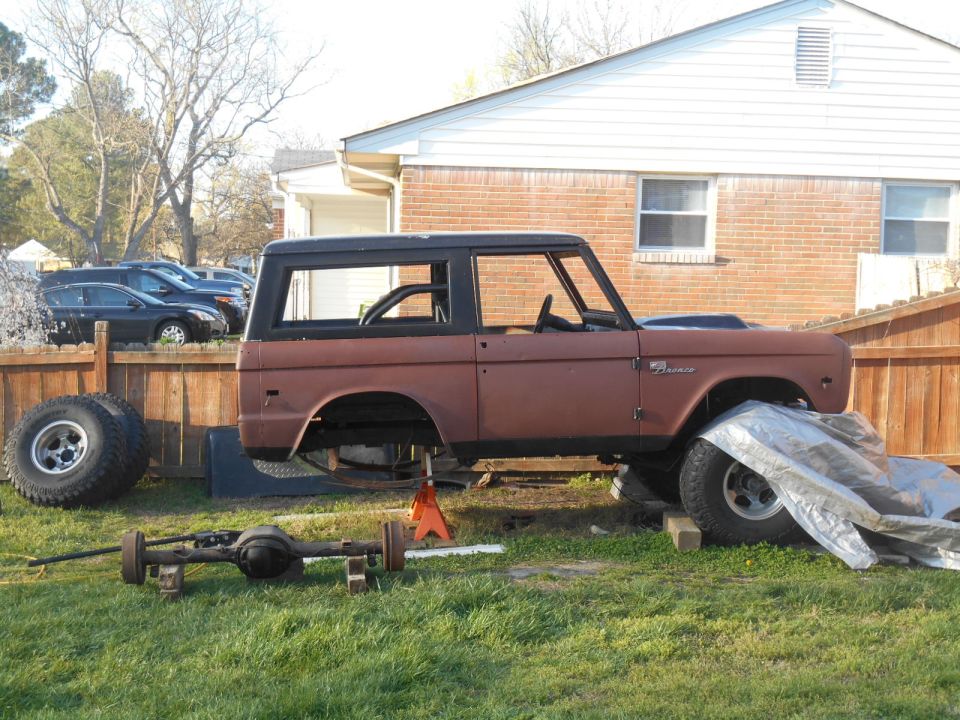 1972 Ford Bronco body on jack stands with a separate axle in the foreground, outdoors.
