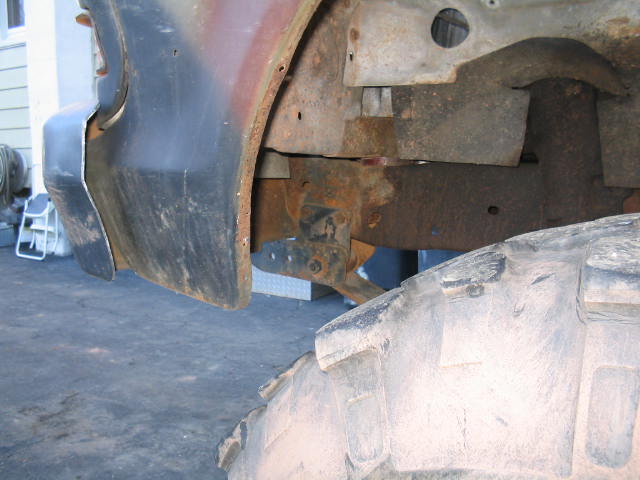Rusty frame rail and bolted leaf spring front hanger bracket behind a mud tire