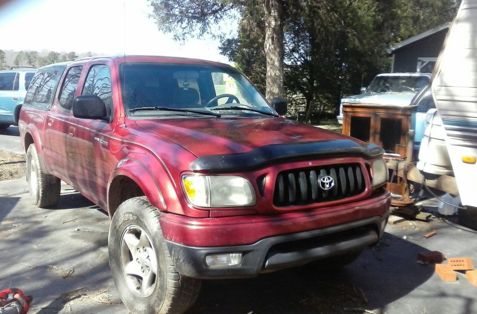 Red Toyota Tacoma pickup truck with a black bug deflector and camper shell.