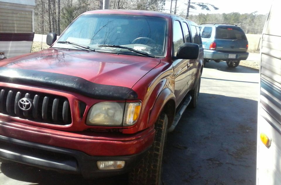 Red Toyota Tacoma pickup truck, front passenger side view, parked next to RV.