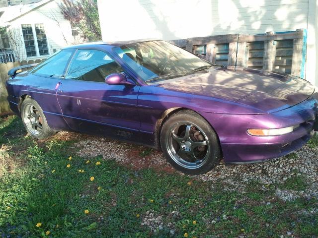 Purple 1995 Ford Probe GT parked on gravel with grass and yellow flowers.