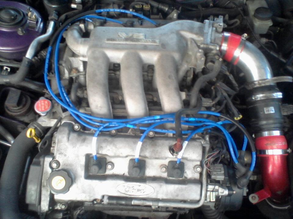 Ford V6 engine bay with blue spark plug wires and red air intake.