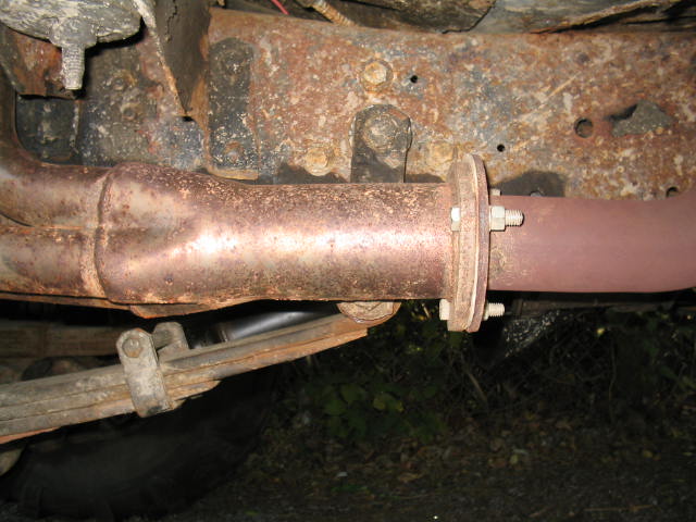 Underside view of rusty exhaust flange, frame rail and leaf spring shackle