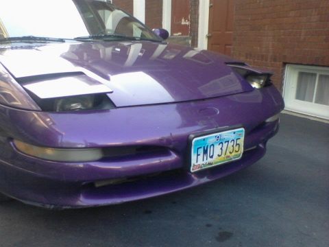 1995 Ford Probe - The front of a purple 1995 Ford Probe is shown parked in front of a brick building. The car has its headlights in the closed position and a…