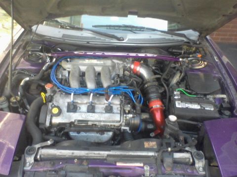 1995 Ford Probe - The engine bay of a purple 1995 Ford Probe is shown with the hood open. Visible modifications include a purple strut bar and red intake pip…